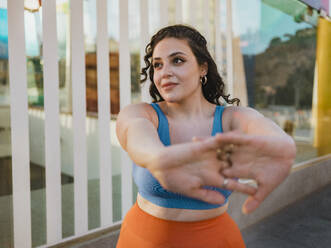 Young woman in sports clothing stretching arms near building - MFF09406