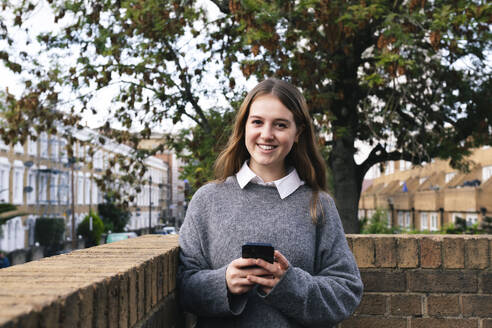 Lächelnde junge Frau mit Smartphone in der Hand - AMWF01941