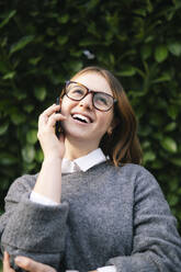 Glückliche junge Frau mit Brille, die mit einem Mobiltelefon spricht - AMWF01945