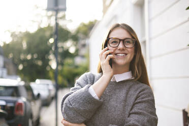 Glückliche junge Frau mit Brille, die mit einem Mobiltelefon spricht - AMWF01946