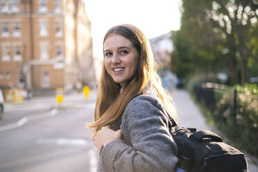 Lächelnde junge Frau mit Rucksack auf der Straße stehend - AMWF01954