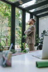 Thoughtful businessman looking through window in office - YTF01267