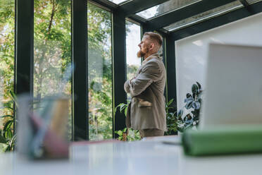 Contemplative businessman looking through window in office - YTF01268