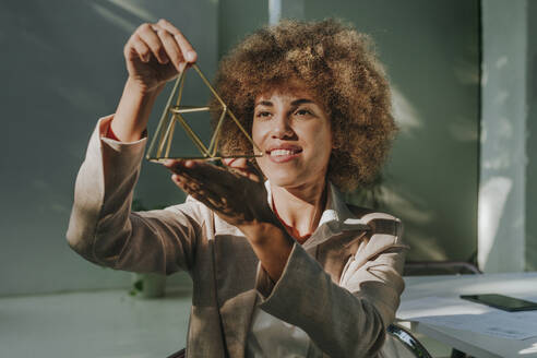 Happy businesswoman examining metal pyramid in office - YTF01281
