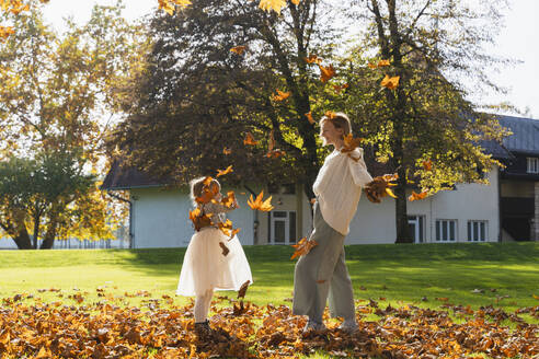 Glückliche Mutter und Tochter spielen mit Herbstblättern vor dem Haus - NDEF01327