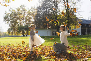 Glückliche Mutter und Tochter spielen mit Herbstblättern an einem sonnigen Tag - NDEF01328