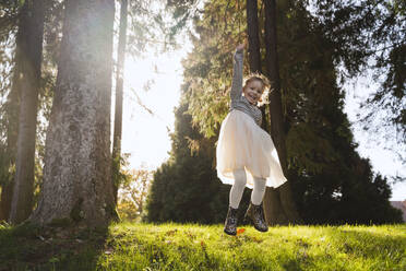 Cheerful girl jumping near trees in forest on sunny day - NDEF01333