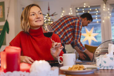 Nachdenkliche blonde Frau mit Rotwein beim Weihnachtsessen zu Hause - NDEF01381