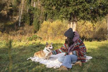 Junge Frau beim Händeschütteln mit Hund auf Decke im Naturpark am Wochenende - VBUF00475