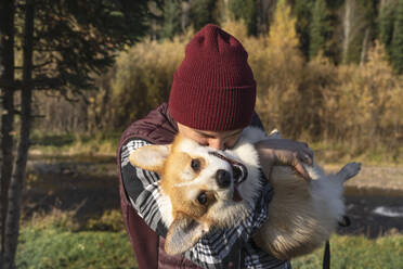 Mann mit Strickmütze küsst glücklichen Hund im Park am Wochenende - VBUF00476