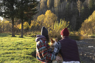 Couple with Pembroke welsh corgi sitting by riverbank in park - VBUF00482