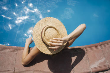 Frau mit Strohhut entspannt sich im Pool an einem sonnigen Tag - YBF00280