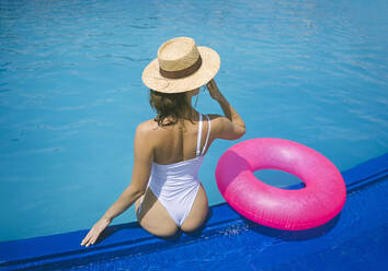 Woman in swimwear relaxing near inflatable swim ring by pool - YBF00283