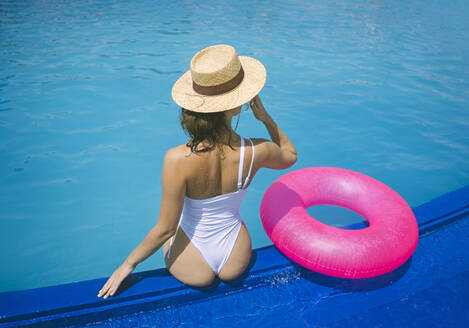 Frau in Badekleidung entspannt sich in der Nähe eines aufblasbaren Schwimmrings am Pool - YBF00283