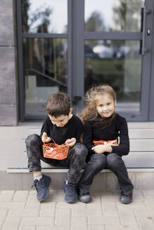 Geschwister sitzen auf dem Gehweg und halten Körbe für Halloween-Süßigkeiten - ONAF00642