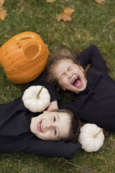 Excited siblings lying on grass with pumpkins - ONAF00652