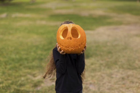 Girl covering face with carved pumpkin - ONAF00653