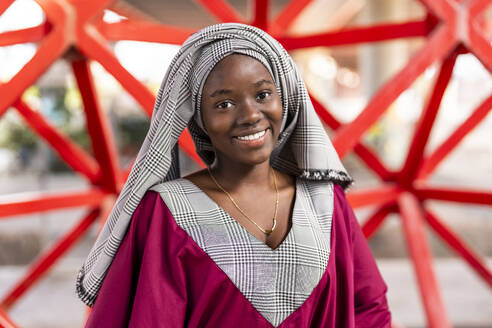 Lächelnde junge Frau mit Hidschab vor einem Geländer stehend - DLTSF03659