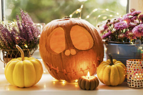 Halloween decoration of Jack O' Lantern with pumpkins and flowers near candle on window sill - ONAF00655