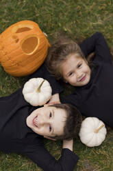 Junge und Mädchen liegen zu Halloween im Gras bei Kürbissen - ONAF00658