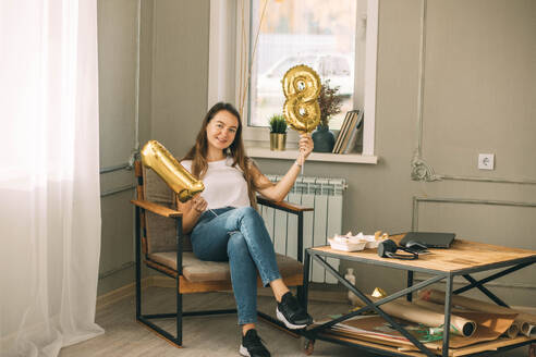 Young woman holding golden number 18 balloons at home - ADF00234