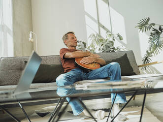 Mann mit Gitarre sitzt zu Hause auf dem Sofa - MFF09431