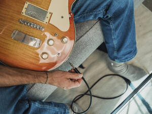 Man plugging cable in guitar at home - MFF09432