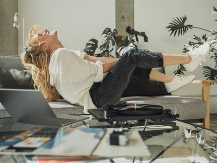 Cheerful woman having fun listening to music through turntable at home - MFF09435