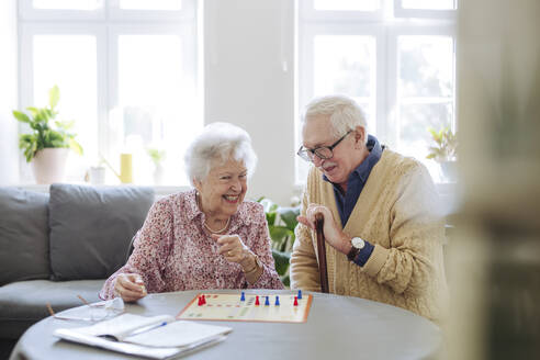 Happy senior woman playing ludo game with man at table in living room - HAPF03226