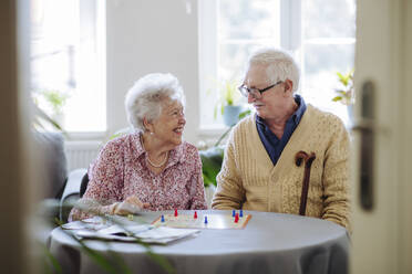 Smiling senior woman playing ludo game with man at home - HAPF03227