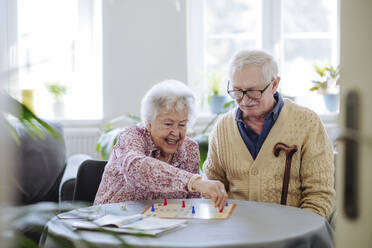 Smiling senior woman playing board game with man at table - HAPF03228