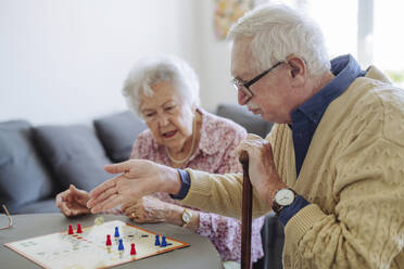 Älterer Mann gestikuliert und spielt Ludo mit Frau zu Hause - HAPF03232