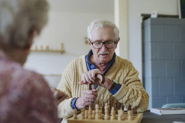 Senior man playing chess game with woman at home - HAPF03237