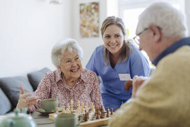 Happy healthcare worker with senior couple playing chess - HAPF03240