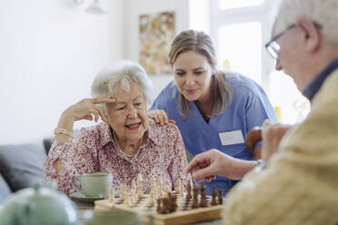 Lächelnde Pflegekraft mit älterem Paar beim Schachspielen - HAPF03241