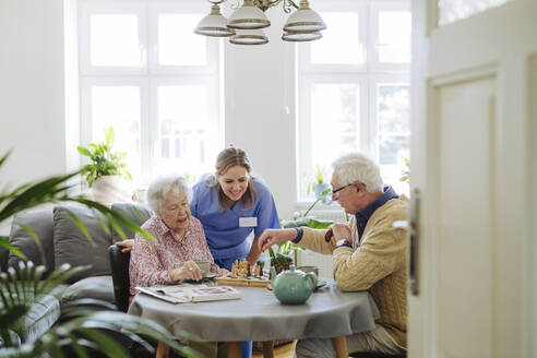 Lächelndes Pflegepersonal mit einem älteren Paar, das am Tisch Schach spielt - HAPF03243