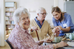 Glückliche ältere Frau mit einer Pflegekraft, die einem Mann im Hintergrund hilft - HAPF03246
