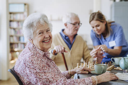 Happy senior woman with healthcare worker assisting man in background - HAPF03246