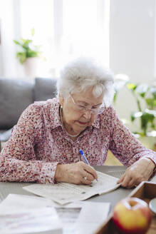 Ältere Frau mit Stift macht Kreuzworträtsel in Buch zu Hause - HAPF03250