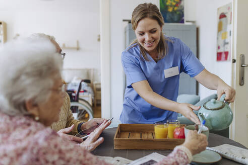 Smiling healthcare worker serving tea to senior couple - HAPF03257