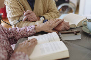 Älteres Paar mit Buch tröstet sich gegenseitig am Tisch - HAPF03262