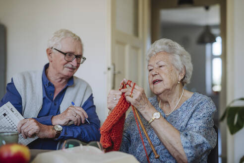 Ältere Frau strickt mit einem lächelnden Mann, der am Tisch sitzt - HAPF03270