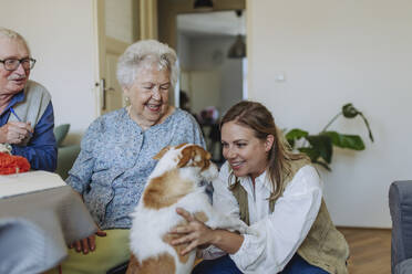 Glückliches älteres Ehepaar mit Pflegerin, die den Hund zu Hause streichelt - HAPF03274