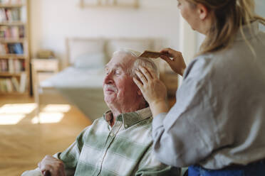 Mitarbeiter des Gesundheitswesens kämmt die Haare eines älteren Mannes im Schlafzimmer zu Hause - HAPF03279