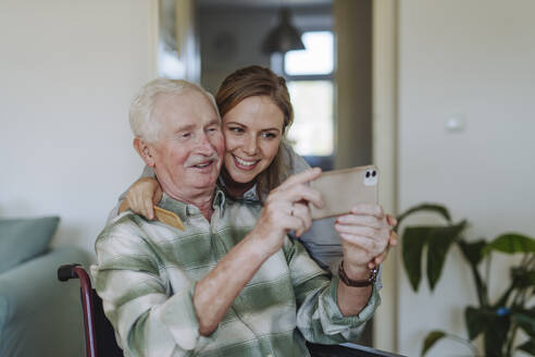 Smiling healthcare worker with senior man taking selfie at home - HAPF03281