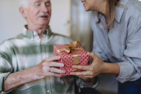 Smiling healthcare worker giving gift to senior man at home - HAPF03286