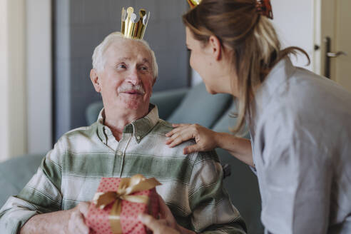 Smiling healthcare worker with man holding gift and celebrating birthday at home - HAPF03287