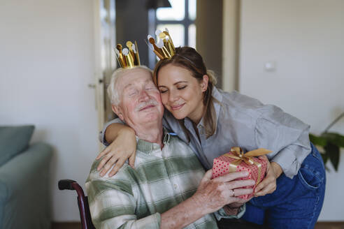 Lächelndes Gesundheitspersonal, das einen Mann zum Geburtstag umarmt und ihm ein Geschenk macht - HAPF03288