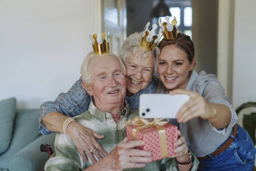 Happy healthcare worker taking selfie with senior couple and celebrating birthday at home - HAPF03291