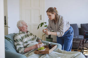 Gesundheitspersonal gibt einem Mann, der zu Hause mit einem Tablett Essen sitzt, Medikamente - HAPF03300